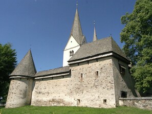 A historic building with a central tower and two smaller towers, surrounded by greenery.