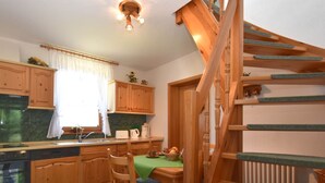 A kitchen with wooden cabinets, a dining table with chairs, a staircase, and a window with curtains. - Sophisticated Holiday Home With Garden (Grabfeld)