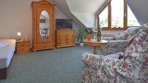 A cozy attic bedroom with a bed, a wooden cabinet, a television, a floral sofa, a small table with a vase, and a window with a view of greenery. - Sophisticated Holiday Home With Garden (Grabfeld)