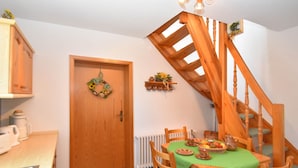 A dining area with a wooden table, chairs, and a green tablecloth. There is a wooden staircase to the right and a door with a wreath. - Sophisticated Holiday Home With Garden (Grabfeld)