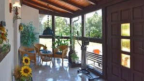 A sunlit room with wooden ceiling beams, wicker furniture, and a treadmill. - Sophisticated Holiday Home With Garden (Grabfeld)