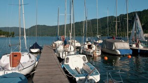 Una marina con diversi natanti ormeggiati, un molo di legno e delle colline sullo sfondo.