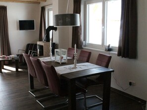 A dining area with a table set for four, surrounded by chairs. A television is mounted on the wall, and a lamp hangs above the table. - Chalet in ski Area in Koetschach-mauthen (Kotschach-Mauthen)