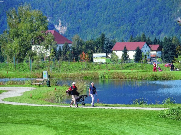 A lakeside path with a bench, a sign, and a small building in the background. - Chalet in Kotschach Near Family Ski Area (Kotschach-Mauthen)
