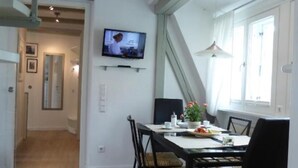 Zona pranzo con tavolo in legno, sedie nere e televisore montato a parete.