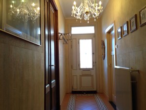 A hallway with a chandelier, a door with a window, and a radiator.