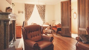 Een ruime woonkamer met een grote leren fauteuil, houten vloeren, een open haard en uitzicht door dunne gordijnen op een helder raam.