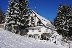 Eine zweistöckige Chalet mit einem steilen Walmdach, umgeben von schneebedeckten Bäumen.