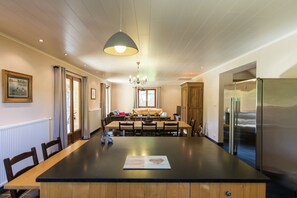 A modern kitchen with a large island, wooden cabinetry, a stainless steel refrigerator, and a dining area with a table and chairs.