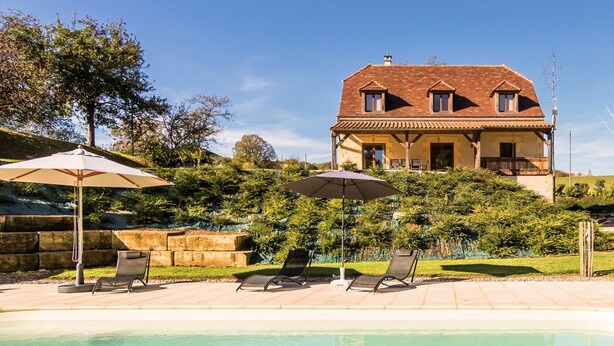 Una casa con piscina, sillas de descanso y sombrillas.