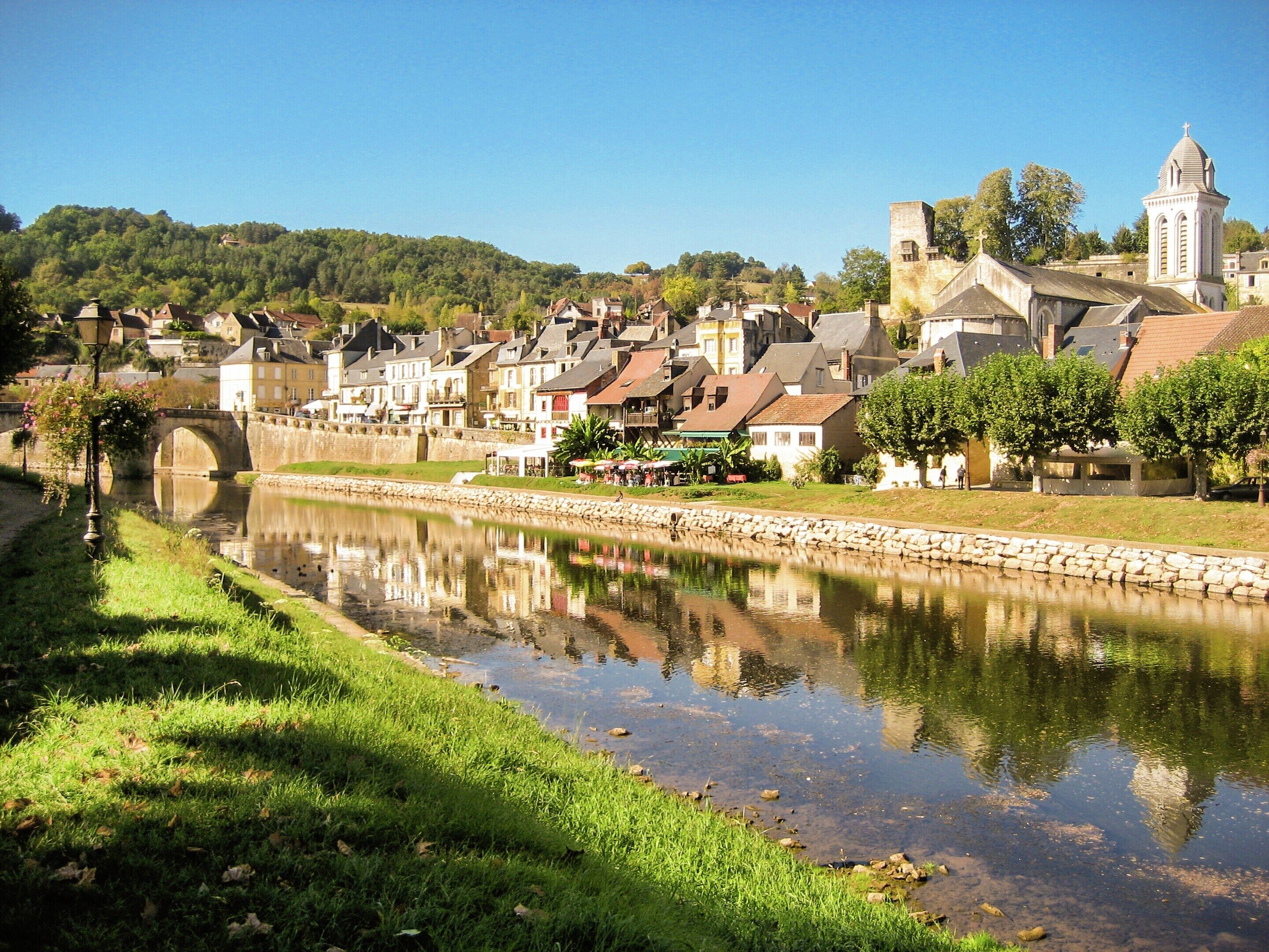 A river with a stone bridge, a town with historic buildings, and a church with a bell tower.