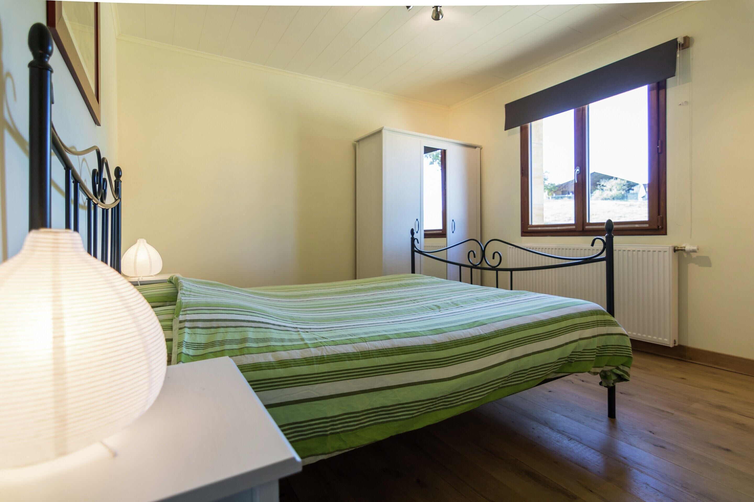 A bedroom with a bed, bedside table, lamp, wardrobe, and window.