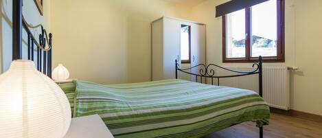 A bedroom with a bed, bedside table, lamp, wardrobe, and window.