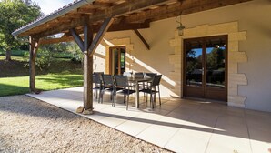 Un patio cubierto con una mesa, sillas, un muro de piedra y una puerta.