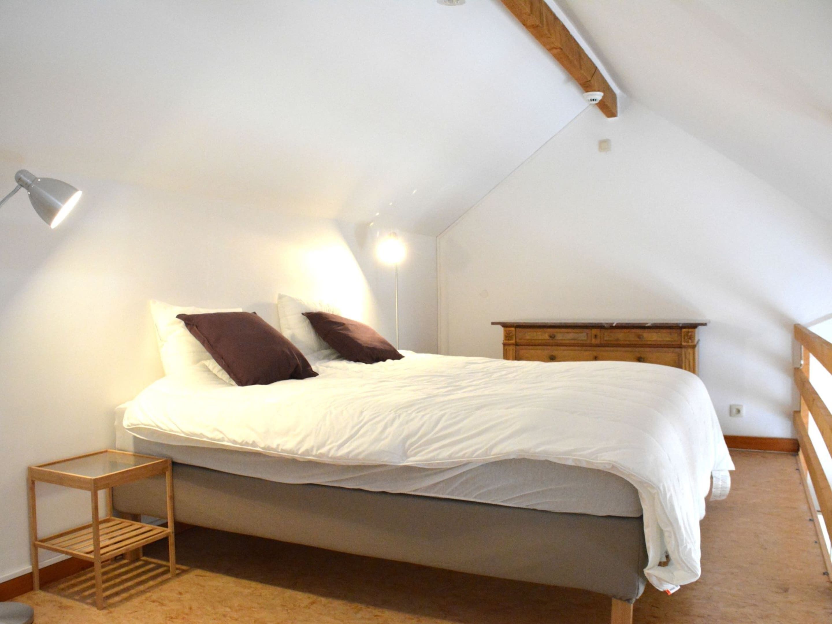 A bedroom with a bed, a bedside table, a lamp, and a dresser.