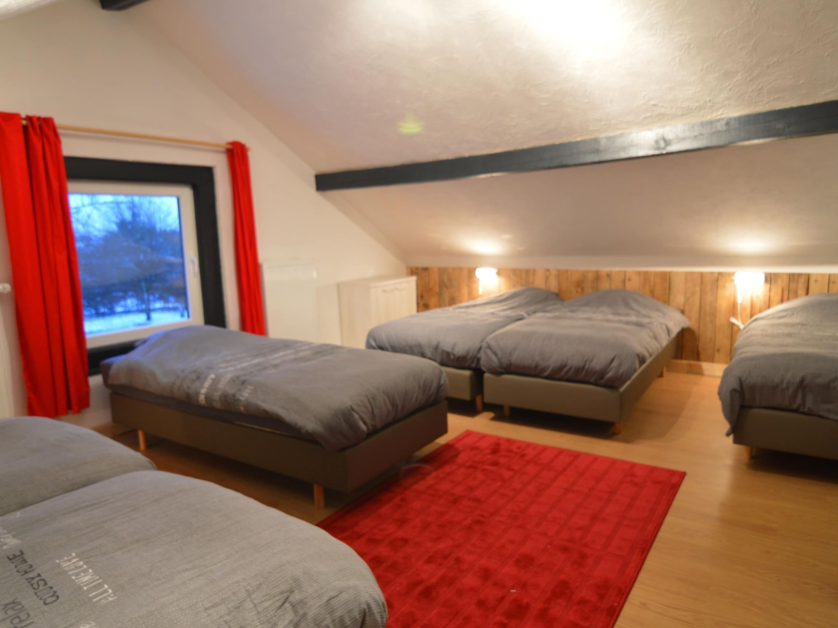 A bedroom with two beds, a red rug, and a window with curtains.