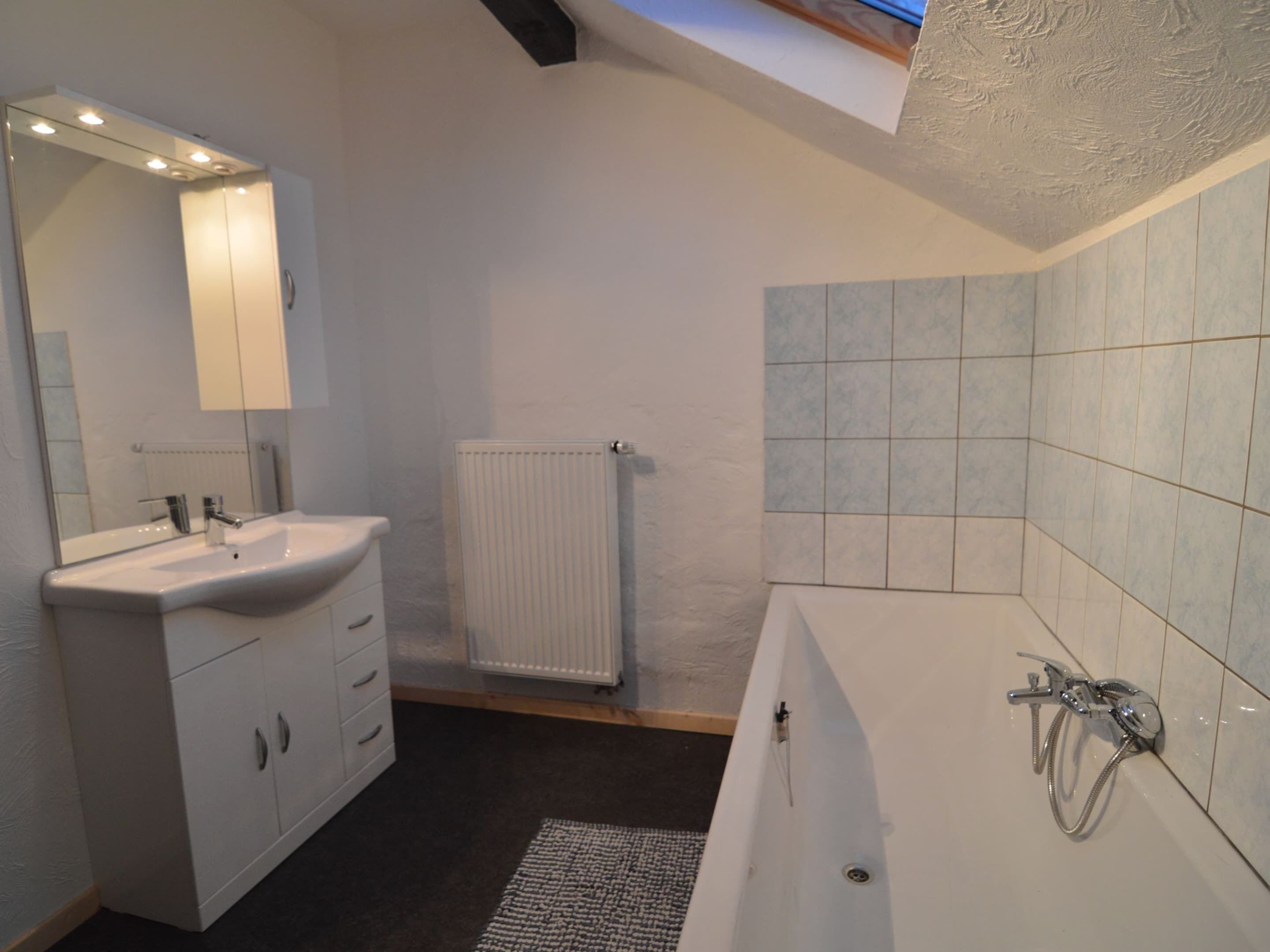 A modern bathroom with a white sink, vanity, and bathtub.