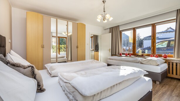 A modern bedroom with a large bed, a wardrobe, and a window with a view of a mountain. - Herzerl-Chalet Appartements (Flachau)