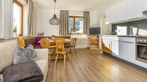 A modern kitchen with white cabinets, a built-in oven, and a dining area with wooden chairs and a table. - Herzerl-Chalet Appartements (Flachau)