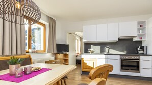A modern kitchen with white cabinets, a built-in oven, and a dining area with a wooden table and chairs. - Herzerl-Chalet Appartements (Flachau)