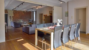 An open-plan living and dining area with a brick wall, wooden flooring, and modern furniture. - House in Former Monastery (Sint-Truiden)