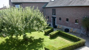 A courtyard with a brick building, neatly trimmed hedges, and outdoor seating. - House in Former Monastery (Sint-Truiden)