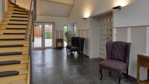 A spacious interior with a wooden staircase, a dark tiled floor, a purple armchair, and a wooden side table. - House in Former Monastery (Sint-Truiden)