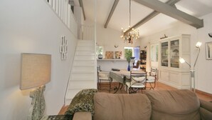 Ein Wohnzimmer mit einer Couch, einem Esstisch mit Stühlen, einer Treppe und einer Chandelier.
