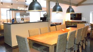 Une cuisine moderne dotée d’un îlot central, d’un coin repas avec des chaises en osier et d’un éclairage suspendu.