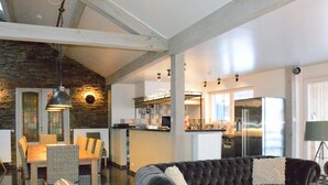 Un vaste espace de vie agrémenté d’un canapé gris foncé, d’une table à manger avec des chaises en osier et d’un mur décoratif en pierre.