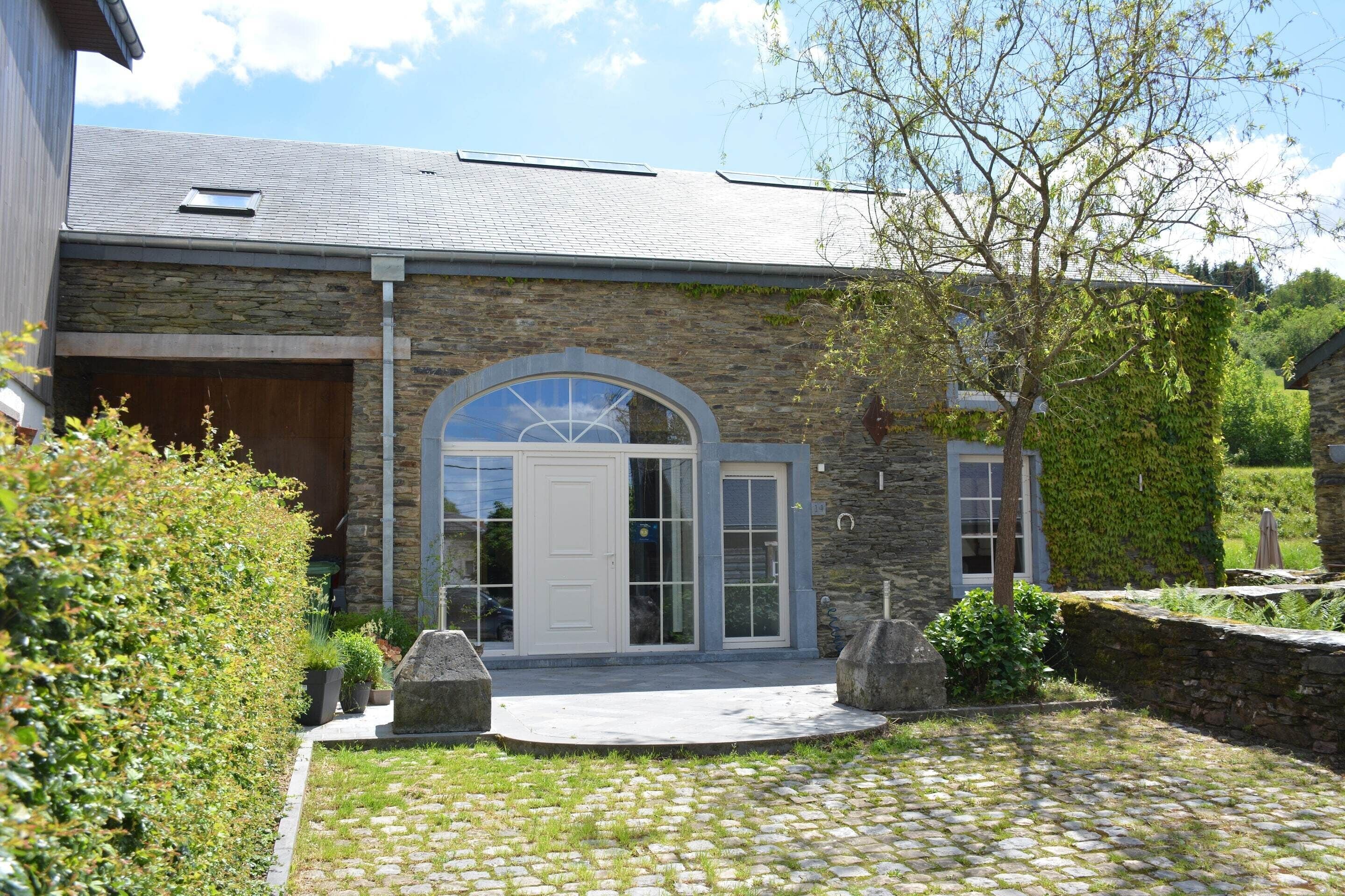 Een gebouw van steen met een grote gewelfde entree, een garage en een bestrate oprit.