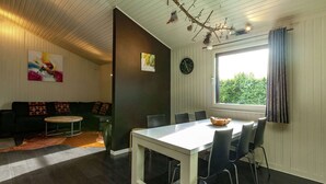 Un salon moderne avec un coin repas, comprenant une table blanche, des chaises noires, un canapé avec des coussins à motifs, une table basse et une branche ornée de décorations suspendues.