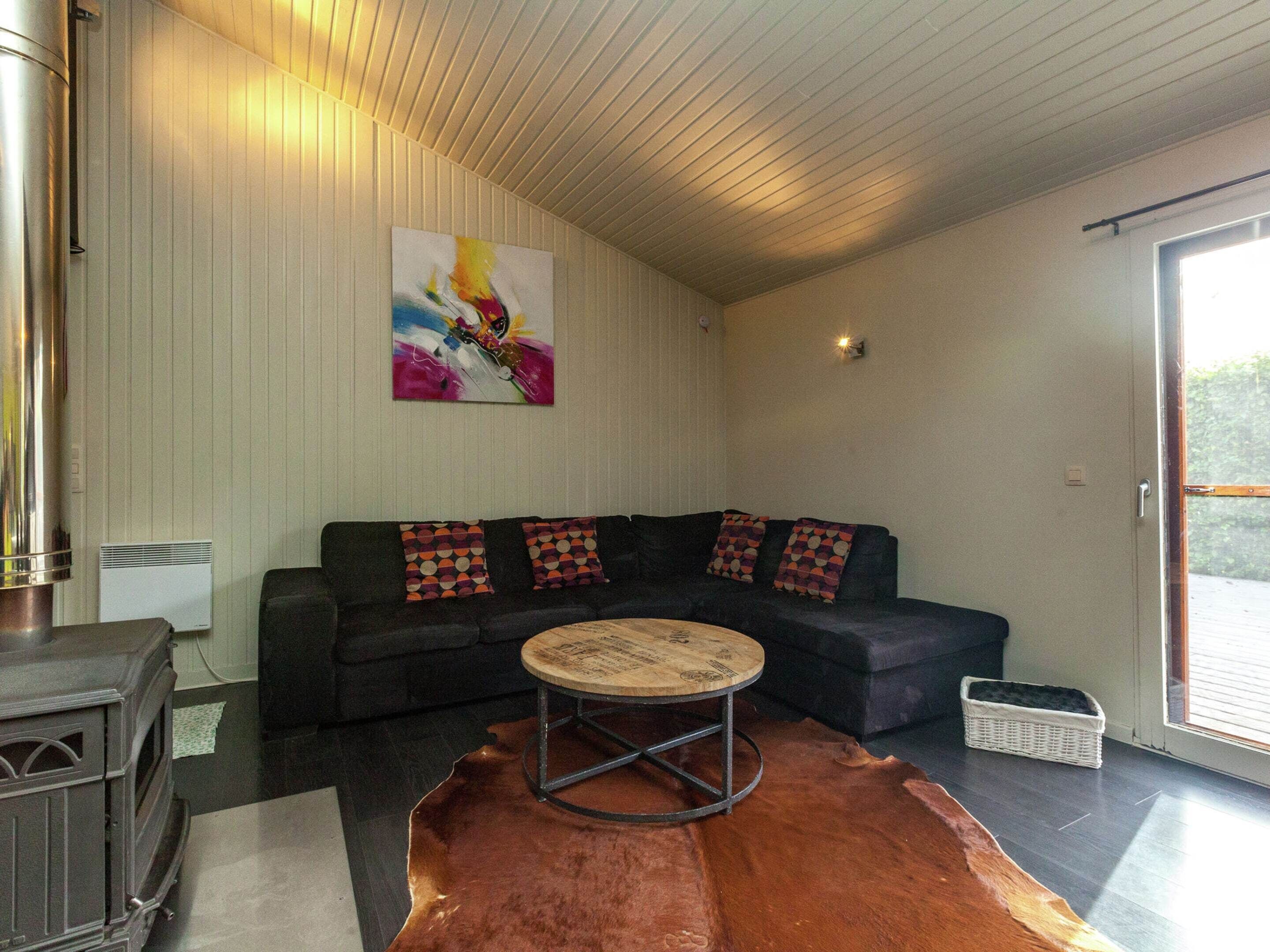 Una sala de estar con un sofá modular, una mesa de centro redonda, un cuadro abstracto grande, una chimenea y un amplio ventanal corredizo al exterior.