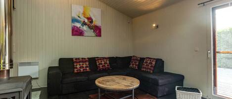 Una sala de estar con un sofá modular, una mesa de centro redonda, un cuadro abstracto grande, una chimenea y un amplio ventanal corredizo al exterior.