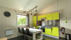 Une cuisine moderne avec des meubles de couleur verte, une table à manger blanche et une horloge noire au mur.