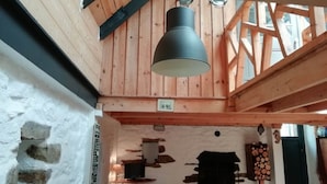A wooden interior with a hanging light fixture, stone wall, and a fireplace. - Brittany Escape With Garden (Cleden-Cap-Sizun)