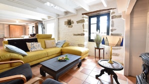 A living room with a yellow sofa, a coffee table, and a stone wall. - Brittany Escape With Garden (Cleden-Cap-Sizun)