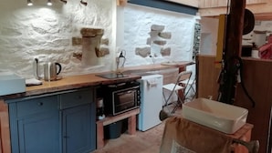A rustic kitchen with stone walls, a wooden countertop, and a small refrigerator. - Brittany Escape With Garden (Cleden-Cap-Sizun)