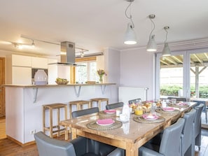 A modern kitchen with white cabinets, a wooden dining table set for breakfast, and a view of the outdoors through large windows. - Quiet Villa with Hot Tub & Sauna (Somme-Leuze)