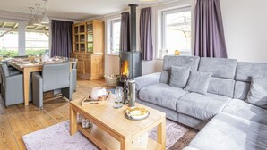 A modern living room with a grey sofa, wooden dining table, and a fireplace. - Quiet Villa with Hot Tub & Sauna (Somme-Leuze)