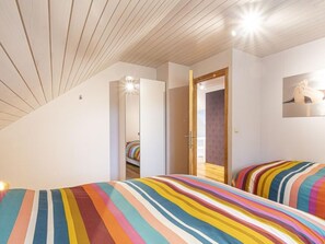 A bedroom with a sloped ceiling, a wooden door, and a bed with striped bedding. - Quiet Villa with Hot Tub & Sauna (Somme-Leuze)
