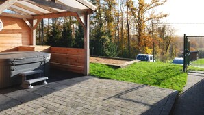 A wooden cabin with a covered patio area, a hot tub, and a view of a forested area. - Quiet Villa with Hot Tub & Sauna (Somme-Leuze)