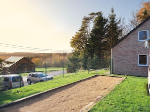 A fenced outdoor area with a dirt track, a brick building with a window, and a wooden cabin in the background. - Quiet Villa with Hot Tub & Sauna (Somme-Leuze)