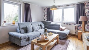 A modern living room with a grey sectional sofa, a wooden coffee table, and a patterned wallpaper. - Quiet Villa with Hot Tub & Sauna (Somme-Leuze)
