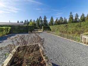 A gravel driveway leading to a wooden gate, surrounded by neatly trimmed hedges and a row of tall trees.