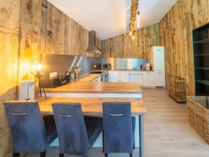 Cozinha moderna com painéis de madeira, exaustor de aço inoxidável e área de jantar com mesa e cadeiras de madeira.