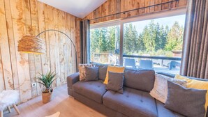 Ein gemütliches Wohnzimmer mit einer Couch, einer Lampe, einer Pflanze und Blick ins Freie.