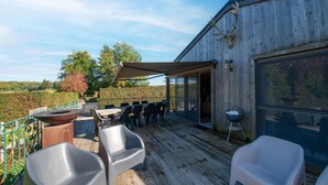 A wooden deck with outdoor seating, a barbecue grill, and a view of the countryside. - Lush Chalet Near Lake of Butgenbach (Buellingen)