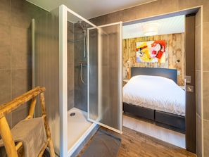 A modern bathroom with a shower, a wooden-framed mirror, and a bed with a headboard.