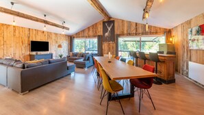 Ein modernes Wohnzimmer mit einer Couch, einem Esstisch mit Stühlen, einem Fernseher und einem großen Fenster.